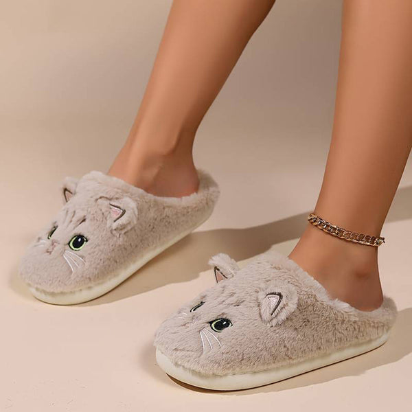 Grijze pluche pantoffels met kattenoortjes en groene ogen, gedragen door een persoon. Comfortabele, warme slippers voor binnengebruik.