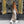 Vrouw in champagnekleurige jurk met open rug, witte sneakers en zwarte handtas voor een moderne architecturale achtergrond. Fashion, street style.
