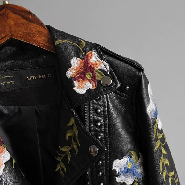 Zwarte leren jas met kleurrijke bloemenborduursels, hangend aan houten hanger. Modieuze damesjas, bikerstijl, trendy kleding, herfstmode.