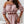 Vrouw in roze off-shoulder crop top en rok, met gouden horloge en armbanden, stijlvolle mode, trendy zomeroutfit, elegante sieraden.