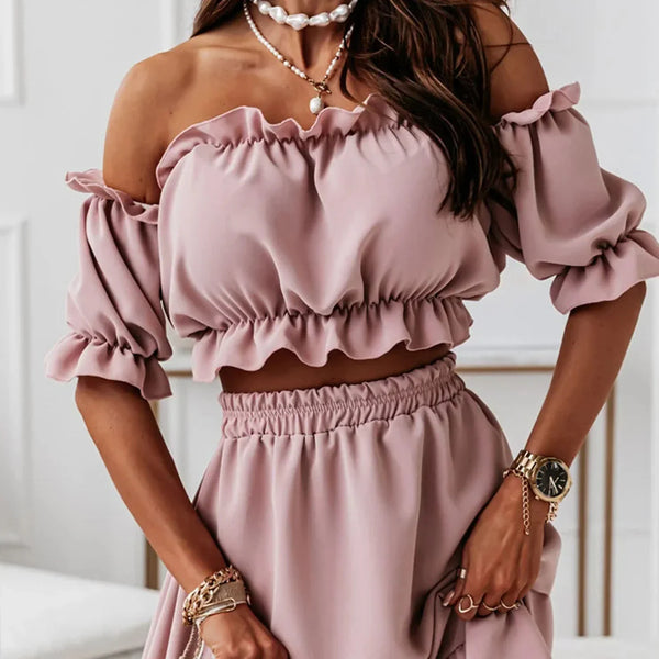 Vrouw in roze off-shoulder crop top en rok, met gouden horloge en armbanden, stijlvolle mode, trendy zomeroutfit, elegante sieraden.