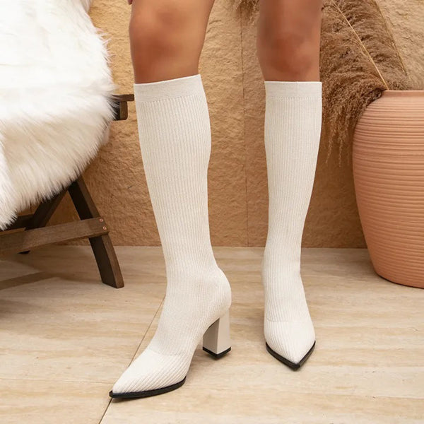 Witte gebreide kniehoge soklaarzen met hoge hakken, gestyled in een moderne interieursetting. Trendy damesmode, herfst/winter schoenen.
