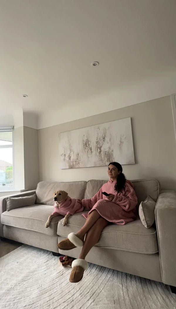 Vrouw en hond in roze dekens op beige bank in moderne woonkamer, ontspannen sfeer, minimalistisch interieur, gezelligheid, huiselijk comfort.