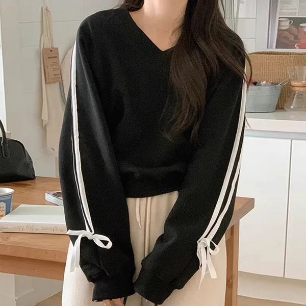 Vrouw in zwarte trui met witte strepen en strikdetails, casual outfit, keukenachtergrond, modieuze dameskleding, comfortabele stijl.