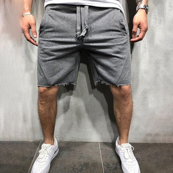 Grijze herenshorts met rafelige zoom, casual stijl, gedragen met witte sneakers. Comfortabele pasvorm, ideaal voor zomerse activiteiten.