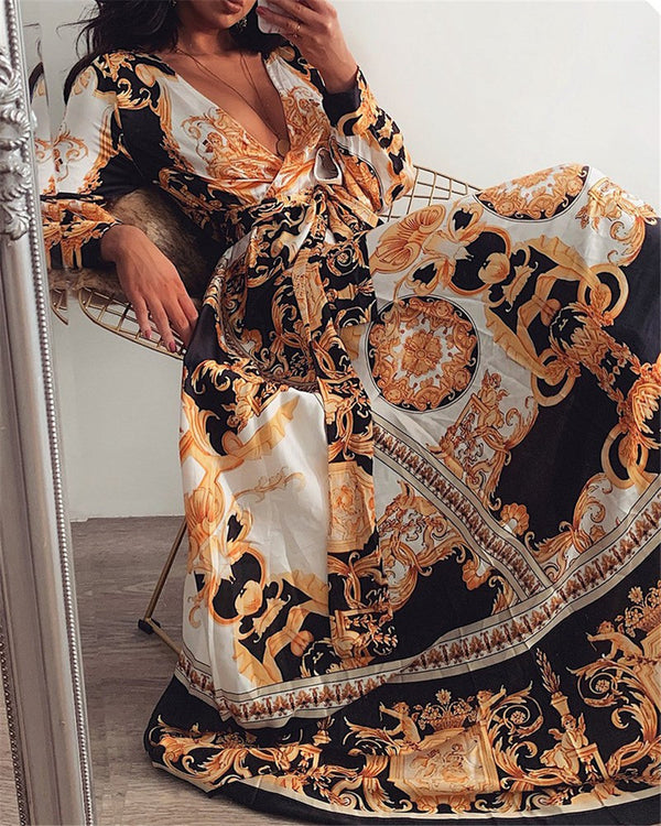Vrouw in elegante, lange jurk met barokke print, zittend op een gouden stoel. Luxe mode, stijlvolle kleding, modetrends 2023.