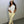 Vrouw in trendy outfit met witte top, beige broek en bucket hat poseert tegen grijze muur. Modieuze streetwear, casual stijl, urban mode.