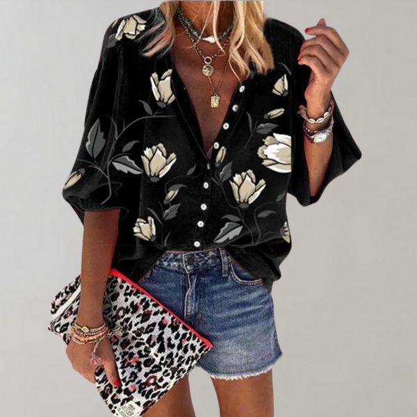 Damesblouse met bloemenprint, zwarte achtergrond, driekwart mouwen, gecombineerd met denim shorts en luipaardprint clutch. Perfect voor casual mode.