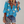Vrouw in blauwe blouse met bloemenprint, korte mouwen en knoopsluiting, gecombineerd met denim shorts en luipaardprint clutch.