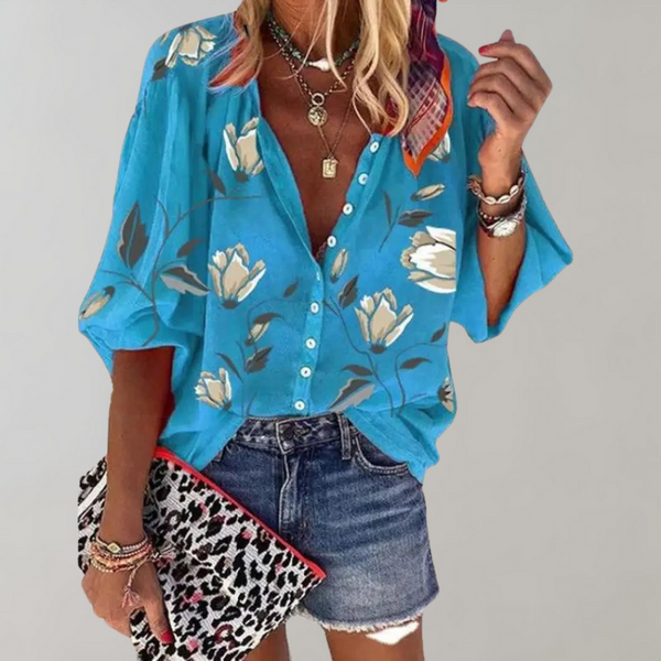 Vrouw in blauwe blouse met bloemenprint, korte mouwen en knoopsluiting, gecombineerd met denim shorts en luipaardprint clutch.