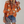 Oranje damesblouse met bloemenprint, driekwart mouwen en knoopsluiting, gecombineerd met denim shorts en luipaardprint clutch.