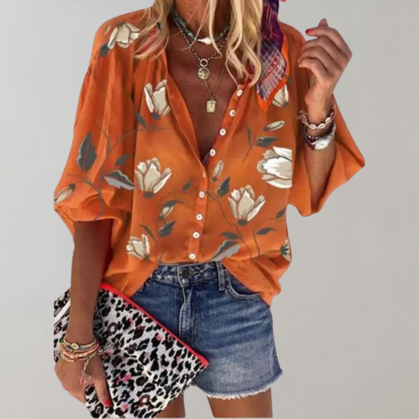 Oranje damesblouse met bloemenprint, driekwart mouwen en knoopsluiting, gecombineerd met denim shorts en luipaardprint clutch.