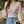 Vrouw in roze-wit gestreepte trui met V-hals en ballonmouwen, draagt blauwe jeans, in moderne keuken. Modieuze dameskleding, casual stijl.
