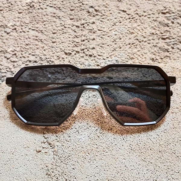 Zwarte zonnebril met geometrisch montuur op ruwe, beige achtergrond. Moderne unisex zonnebril, stijlvol en trendy accessoire.
