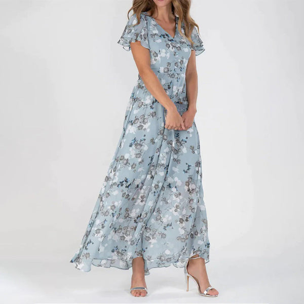 Vrouw in lichtblauwe, bloemenprint maxi-jurk met korte mouwen en V-hals, poseert op witte achtergrond. Elegante damesmode, zomerjurk.