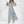 Vrouw in lichtblauwe, bloemenprint maxi-jurk met korte mouwen, houdt een boeket bloemen vast. Perfect voor zomerse evenementen en bruiloften.