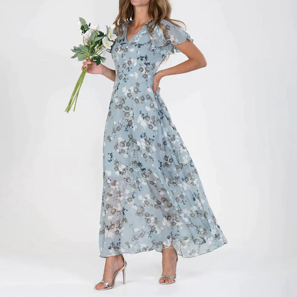 Vrouw in lichtblauwe, bloemenprint maxi-jurk met korte mouwen, houdt een boeket bloemen vast. Perfect voor zomerse evenementen en bruiloften.