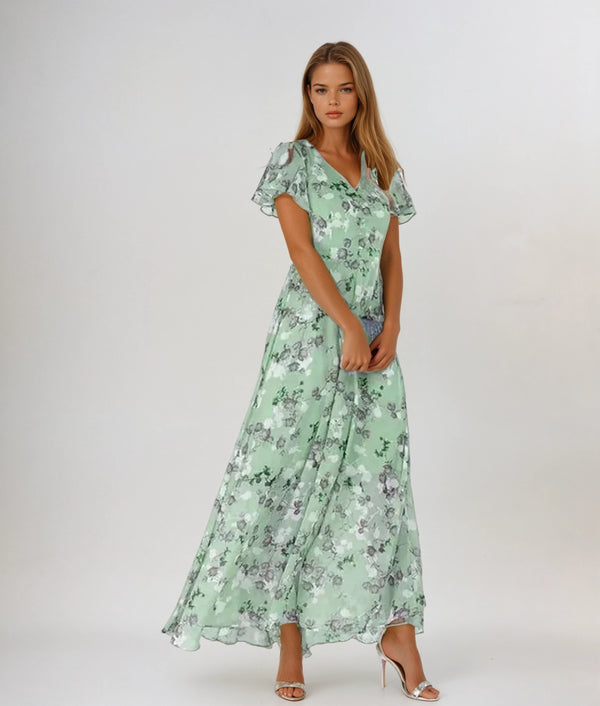 Vrouw in elegante, lange, groene bloemenjurk met korte mouwen en V-hals, poseert op witte achtergrond. Perfect voor zomer- en lentemode.