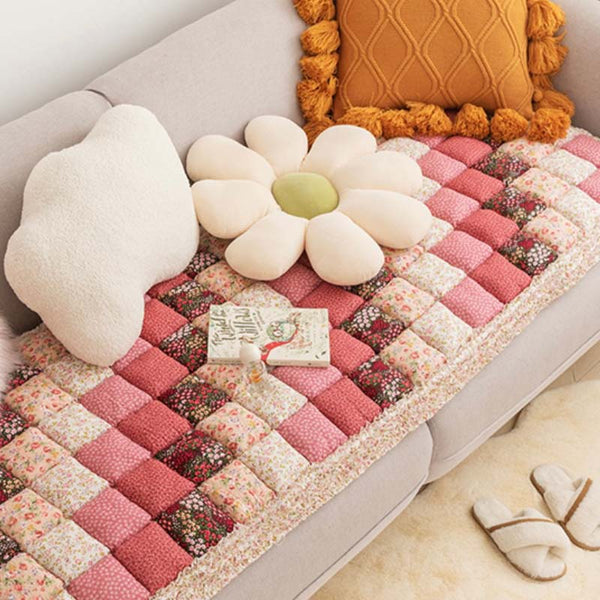 Roze katoenen bankhoes met bloemenpatroon, decoratieve kussens en een boek op een beige bank. Perfect voor stijlvolle woonkamerinrichting.
