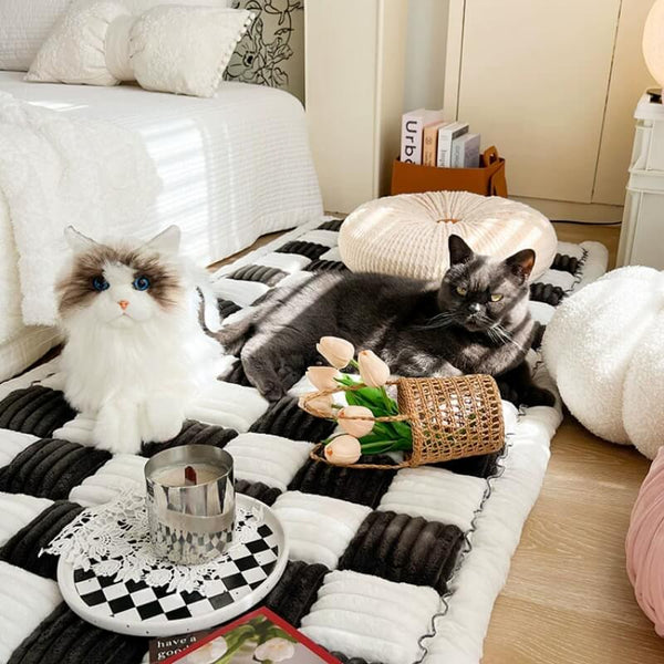 Twee katten op een zwart-wit geruite katoenen bankhoes in een zonnige kamer, met een omgevallen mand tulpen en een kaars op een dienblad.