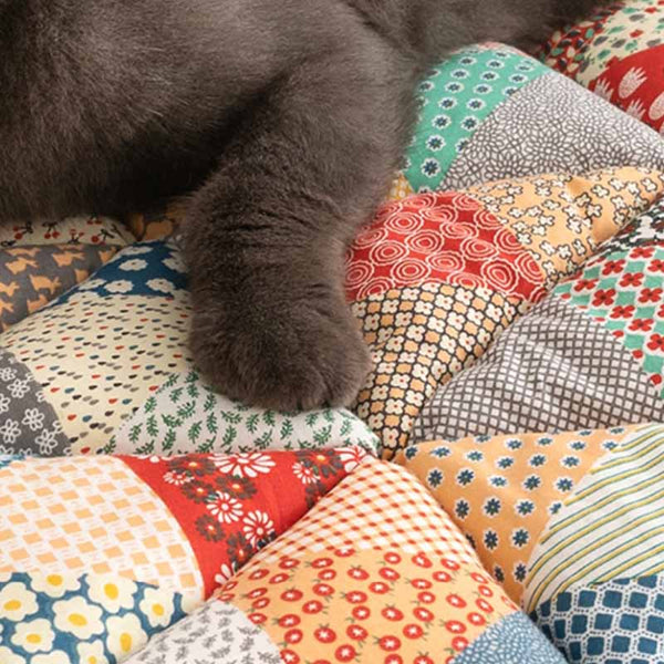 Grijze kat op kleurrijke patchwork bankhoes van katoen, met bloemen- en geometrische patronen. Perfecte bescherming en stijl voor je interieur.