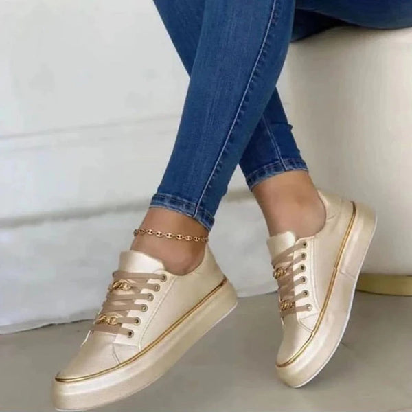 Gouden damessneakers met kettingdetail, gedragen met strakke blauwe jeans. Stijlvolle casual schoenen, trendy modeaccessoire.