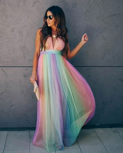 Vrouw in lange regenboogjurk met spaghetti bandjes, haltertop en vloeiende rok. Perfect voor zomerfeesten en gala's. Trendy damesmode.