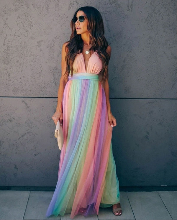 Vrouw in lange regenboogjurk met spaghetti bandjes, haltertop en vloeiende rok. Perfect voor zomerfeesten en gala's. Trendy damesmode.
