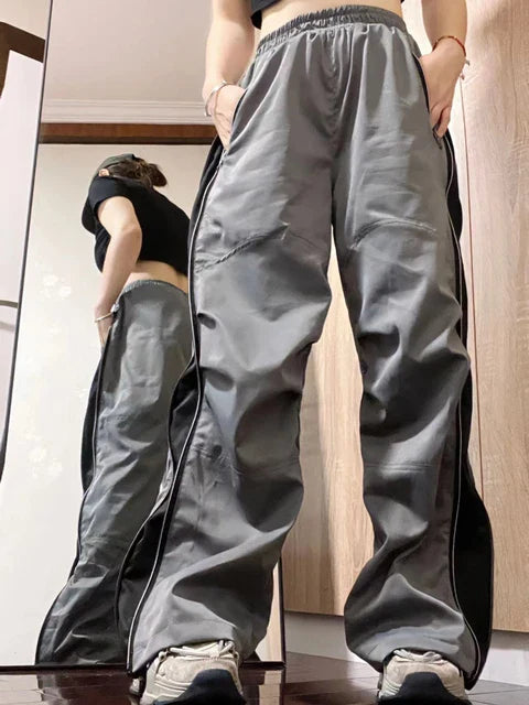 Grijze en zwarte trainingsbroek met wijde pijpen, gedragen door een persoon voor een spiegel. Modieuze sportkleding, comfortabele pasvorm.
