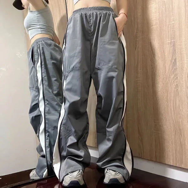 Grijze trainingsbroek met witte strepen, gedragen door een persoon voor een houten kast. Sportieve mode, comfortabele pasvorm, casual stijl.
