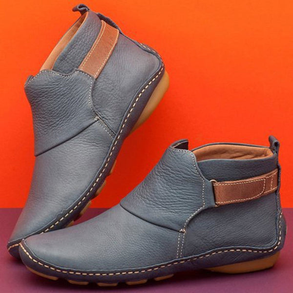 Grijze leren enkellaarsjes met bruine accenten, comfortabele zool, tegen oranje achtergrond. Stijlvolle herenschoenen, casual en modieus.