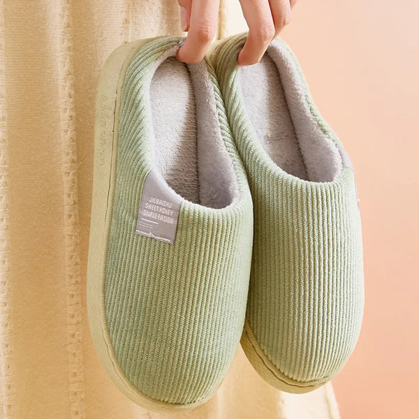 Groene ribfluwelen pantoffels met zachte voering, vastgehouden door een hand. Comfortabele huisschoenen voor dames, ideaal voor dagelijks gebruik.