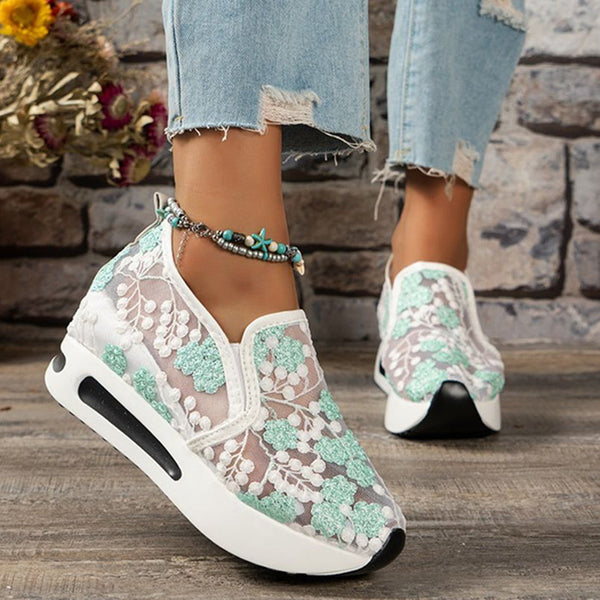 Vrouw draagt trendy sneakers met groene bloemenkant, gecombineerd met gescheurde jeans. Stijlvolle damesmode, casual schoenen, boho-accessoire.