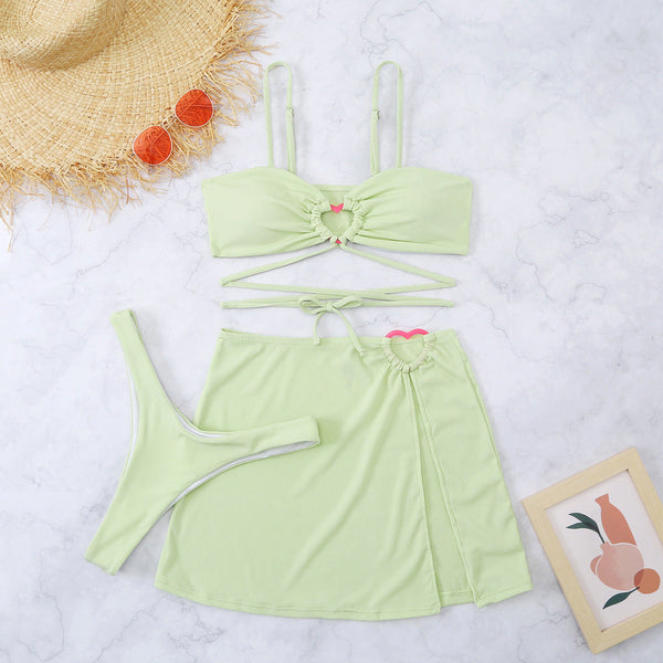 Lichtgroene bikini set met rok en hartdetails, naast een strohoed, oranje zonnebril en kunstprint. Perfect voor zomerse strandmode.