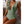 Vrouw in stijlvol groen badpak met diepe V-hals en ruches, zittend op een bank. Perfect voor strandmode en zomertrends.
