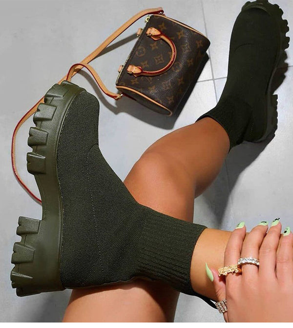 Groene soklaarzen met dikke zolen, gedragen door een persoon met sieraden, naast een designer handtas op een grijze vloer. Trendy modeaccessoires.