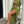 Vrouw in groene jurk met hoge split, poseert op zwart-wit geblokte vloer, draagt beige hakken en zebra tas. Trendy mode, elegante stijl.
