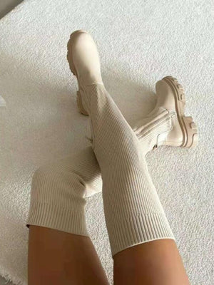 Beige ribgebreide kniehoge laarzen op witte vloer, stijlvolle damesmode, comfortabele herfst- en winterlaarzen, trendy schoeisel.