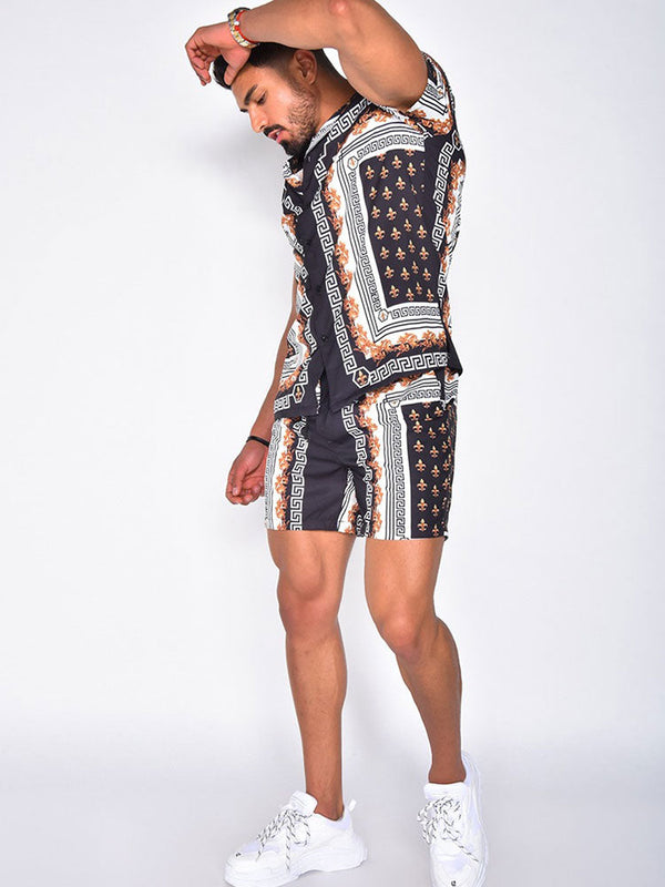 Man in modieuze, zwart-witte barokprint set met korte mouwen en shorts, poseert tegen witte achtergrond. Trendy herenmode, zomeroutfit.