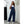 Vrouw in blauwe tuinbroek en witte sneakers, leunend tegen witte muur. Casual mode, dameskleding, comfortabele outfit, buitenfotografie.