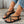 Vrouwelijke voeten met zwarte gevlochten sandalen, jeans met pareldetails en gouden enkelbandjes. Stijlvolle zomerschoenen, casual mode.