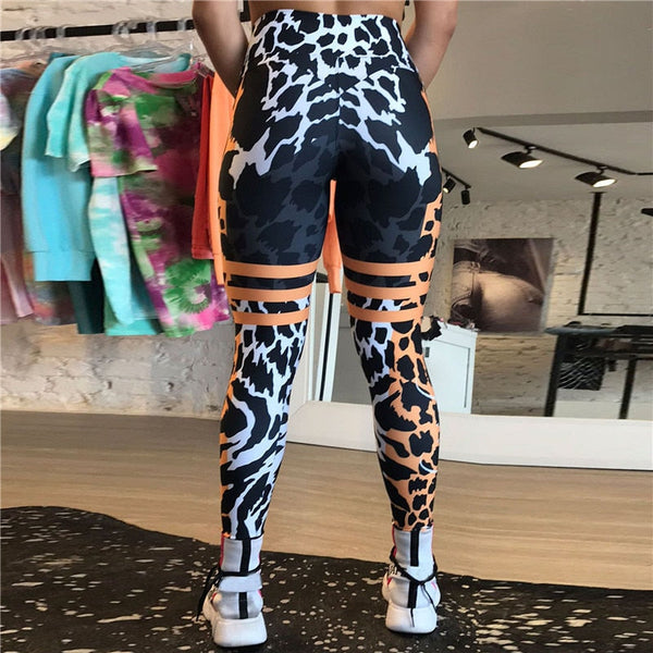 Dames sportlegging met zwart-wit luipaardprint en oranje accenten, hoge taille, in een moderne kledingwinkel. Perfect voor fitness en yoga.
