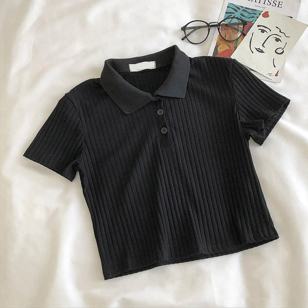 Zwarte geribbelde polo crop top op witte achtergrond, naast een bril en een kunstboek. Trendy dameskleding, casual mode, zomerstijl.