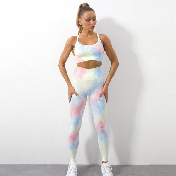 Vrouw in kleurrijke tie-dye sportset, bestaande uit een sportbeha en leggings, poseert tegen een witte achtergrond. Fitnessmode, dames sportkleding.