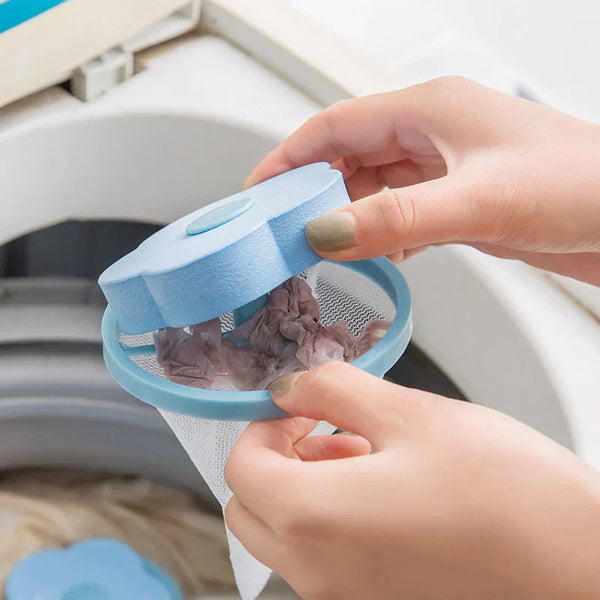 Handen houden een blauwe wasmachine-pluizenfilter in bloemvorm boven een wasmachine. Effectieve pluisverwijderaar voor schone was.