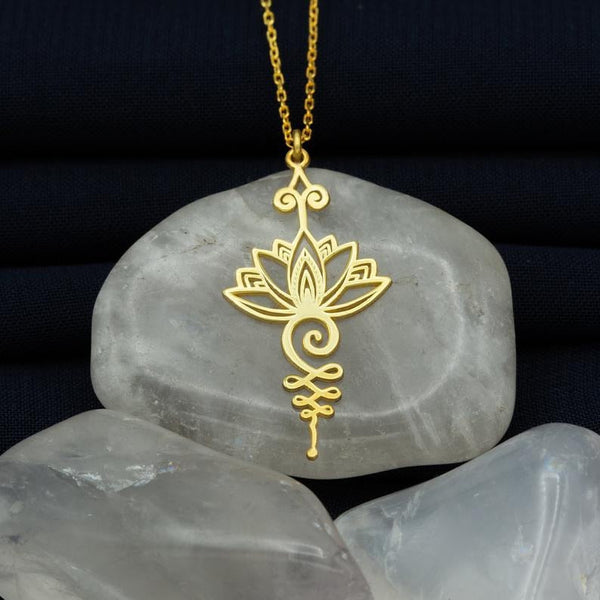 Gouden lotushanger op grijze steen, sieradenfotografie, elegante ketting, spirituele symboliek, minimalistisch design, luxe accessoire.