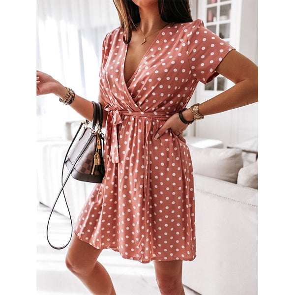 Vrouw in roze polkadot zomerjurk met V-hals en korte mouwen, draagt een zwarte handtas. Perfecte outfit voor casual en trendy zomermode.