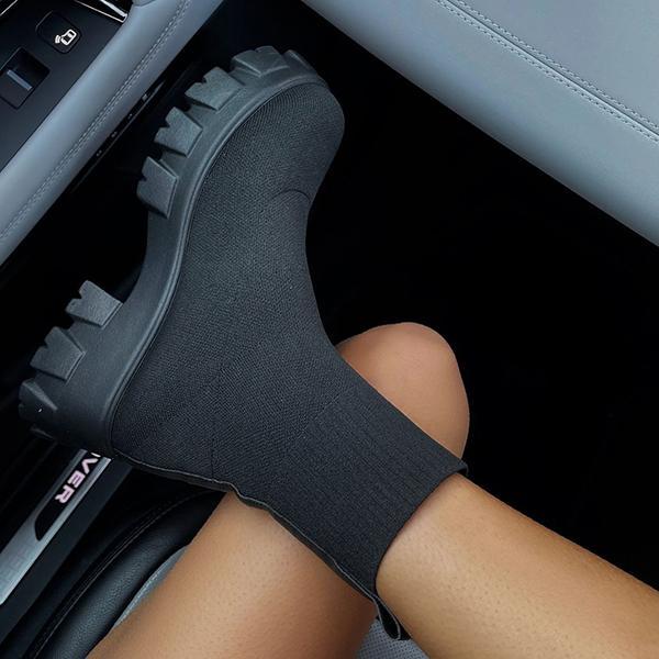 Zwarte enkellaars met dikke zool, gedragen in auto-interieur. Trendy damesmode, comfortabele soklaars, perfect voor casual en stedelijke outfits.