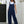 Vrouw in blauwe tuinbroek en witte T-shirt poseert buiten bij witte muur en smeedijzeren poort, casual mode, comfortabele dameskleding.