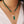 Groene kralenketting met gouden sluiting, parelhanger en groene bladbedel, gedragen op witte blouse. Elegante sieraden voor dames.